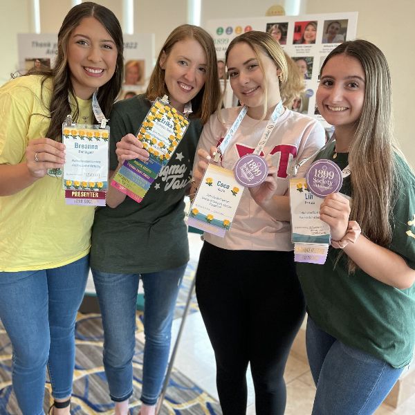 Four members at Convention holding their nametags with yellow rose stickers applied.